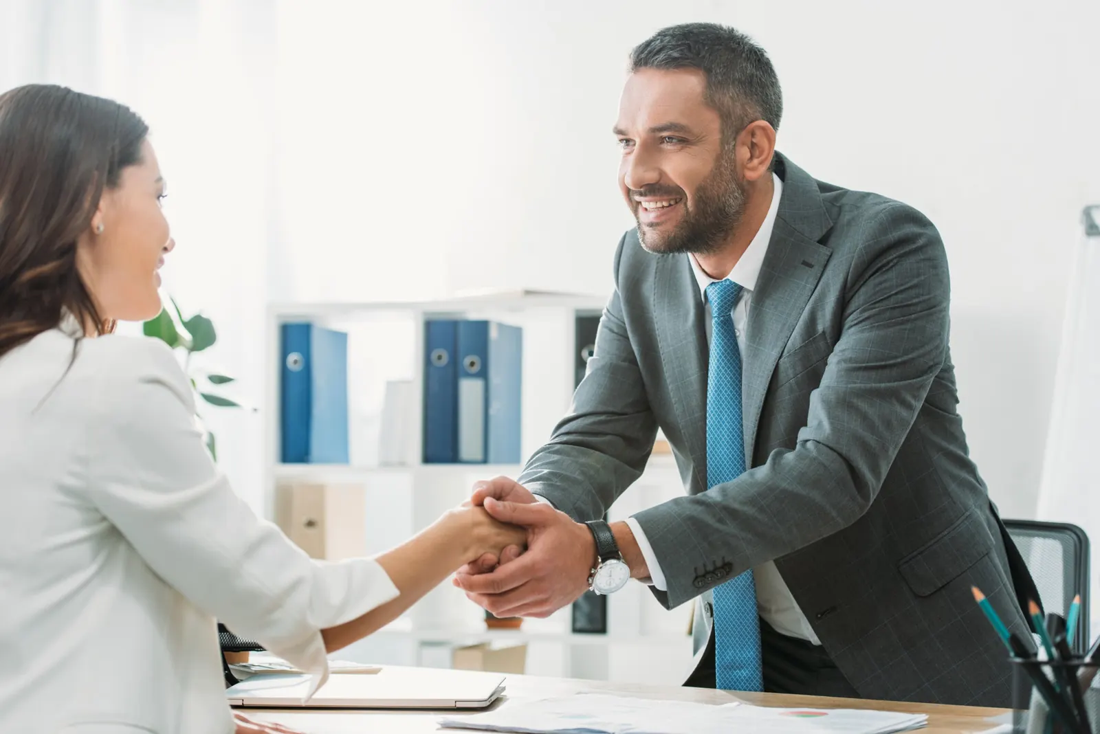 An advisor shaking hands with a client across a desk